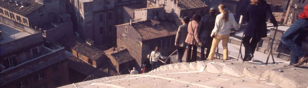 A photo of people climbing down the roof of the Pantheon in Rome and houses and other buildings in the distance.