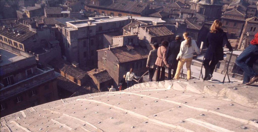 A photo of people climbing down the roof of the Pantheon in Rome and houses and other buildings in the distance.